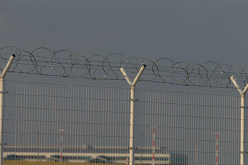 A barbed wire fence stands firmly, silhouetted against a gray, cloudy sky in the background,...