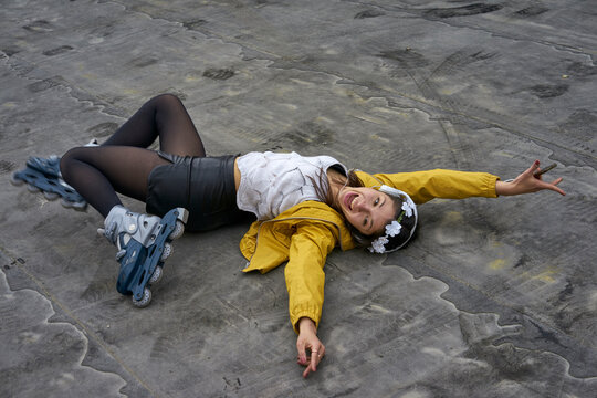 Screaming young woman with inline skates lying on ground listening music with headphones