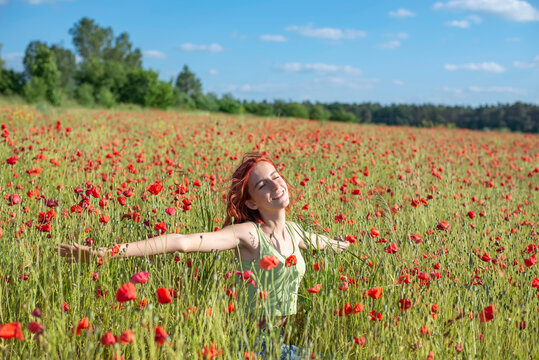 Redhead girl with arms outstretched enjoying at poppy field on sunny day