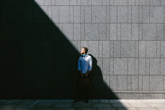 Young businessman standing in front of a grey wall looking up