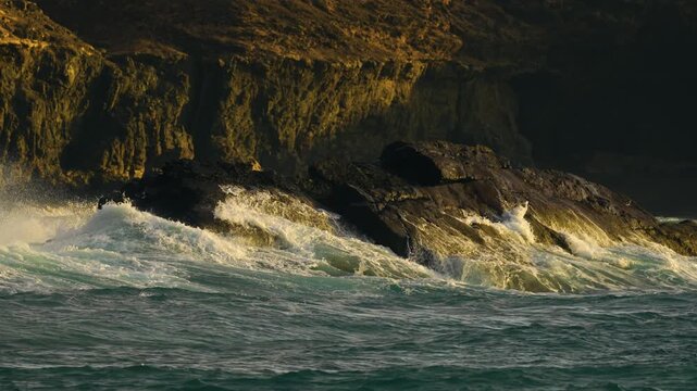 Slow motion close-up of ocean waves crashing on rocky shore at sunset near El Cotillo, Fuerteventura, Canary Islands