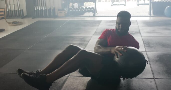 Upon sitting in V-sit, man is twisting medicine ball side to side to build core strength