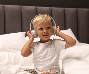 Cute little boy in headphones on bed