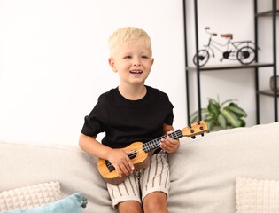 Cute little boy playing toy guitar on sofa at home
