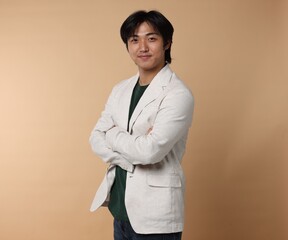Portrait of handsome Asian businessman in suit with crossed arms on beige background