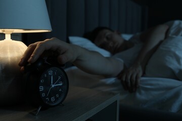 Frustrated man suffering from insomnia in bed indoors, focus on alarm clock