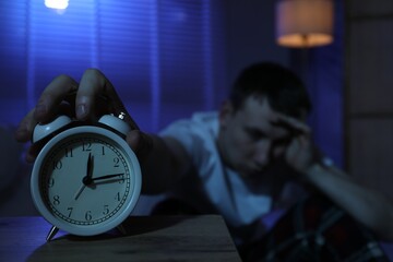 Frustrated man suffering from insomnia indoors, focus on alarm clock
