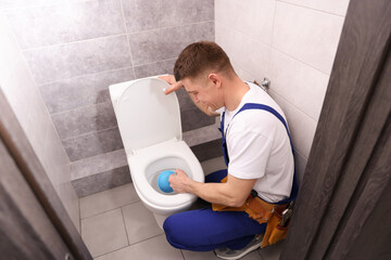 Plumber unclogging toilet with hand plunger indoors