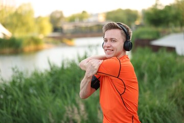 Naklejka premium Smiling sportsman in headphones doing morning exercise outdoors
