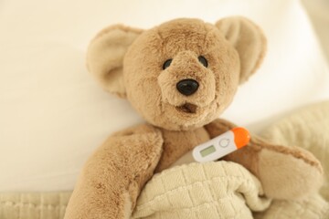 Pediatrics concept. Toy bear with thermometer in bed