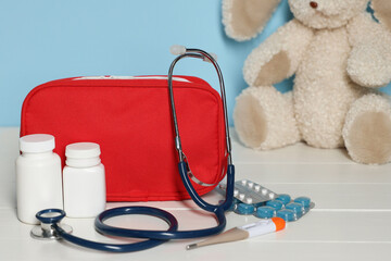 Pediatrician concept. First aid kit, pills, thermometer, stethoscope and toy bunny on white wooden...