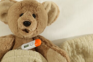 Pediatrics concept. Toy bear with thermometer in bed, closeup. Space for text