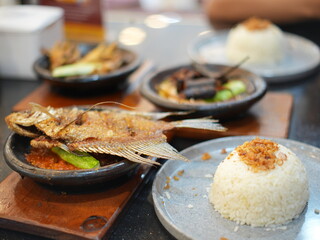 Indonesian traditional food served on a black table. Fried fish, chicken feet, spicy soup, dried beef, and rice with crispy shallots on top.