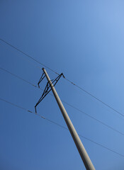 A tall utility pole with electrical wires stretches against a clear blue sky.
