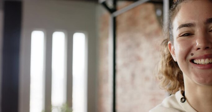 Reacting to prompt, woman in hoodie cycling through smile, laugh, smirk at loft window, copy space