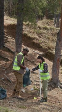 Vertical shot of two volunteers picking bottles and plastic cups with trash pickers and placing them in bags