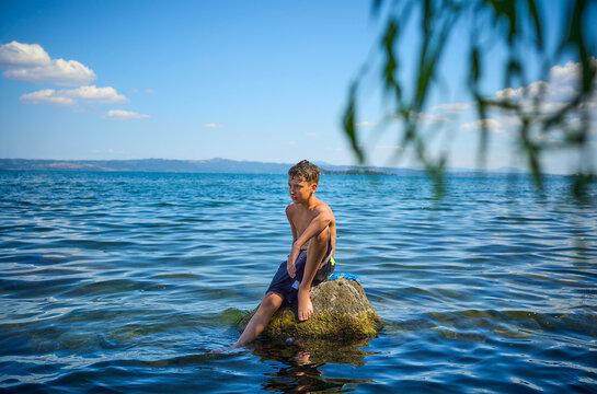 Teenage boy sitting on rock in lake Bolsena, Italy