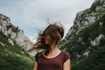 Mid adult woman with tousled long brown hair against mountain range