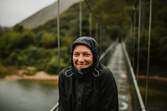 Smiling woman standing on suspension bridge over Sella river on rainy day
