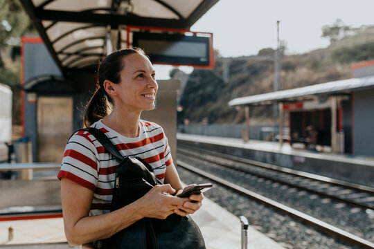 Smiling woman with smart phone standing at railroad station