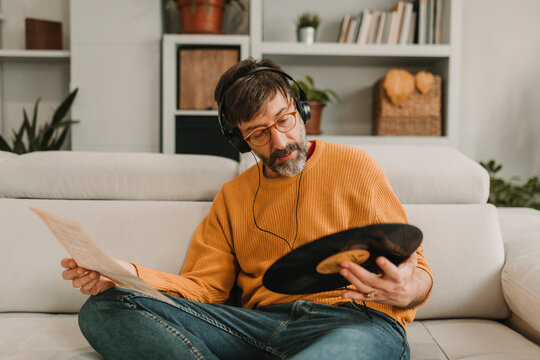 Man listening to music and reading paper holding record sitting on sofa at home