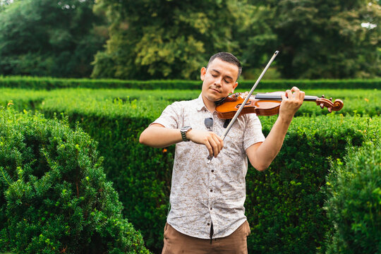 Young man with eyes closed playing violin by plants at park
