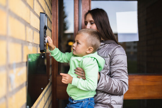 Woman carrying son using intercom outside building