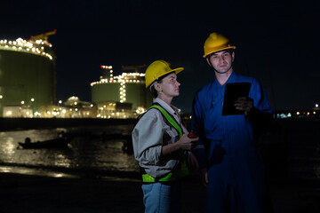 Male and female engineers wearing helmets working at an oil refinery site holding walkie-talkies...