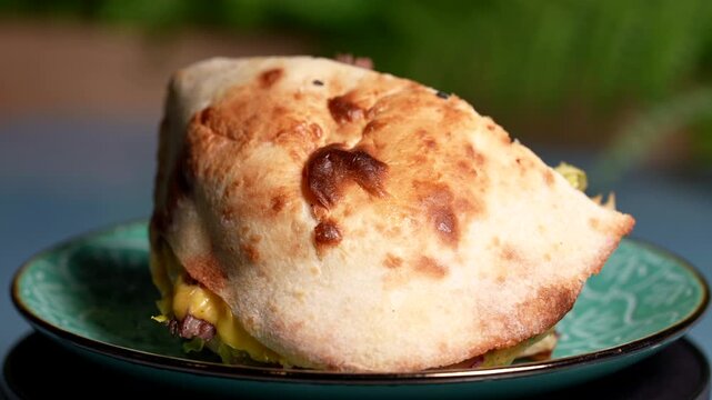 Golden baked flatbread stuffed with melted cheese and beef, served on a green patterned plate.