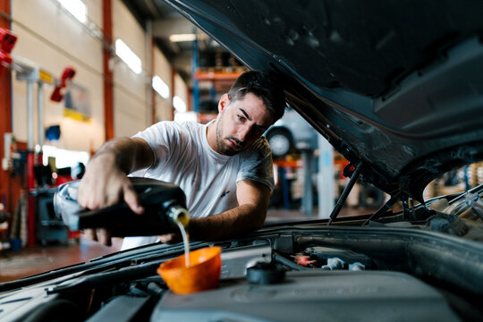 Auto mechanic filling engine oil while standing in garage