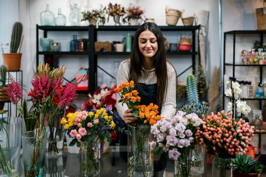 Young female florist arranging flowers at shop