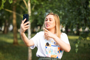 Pretty woman taking selfie with mobile phone looking at camera in a park. Blogger recording video...