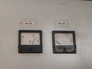 Two analog voltmeters displayed on a grey electrical panel, showing voltage readings.