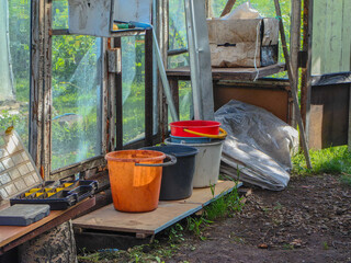 Old greenhouse interior with buckets, tools and rustic details under daylight.