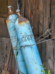 Two old blue gas tanks stand against a weathered wooden wall, showcasing industrial decay.