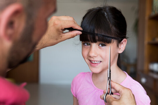 Father cutting daughter's hair at home