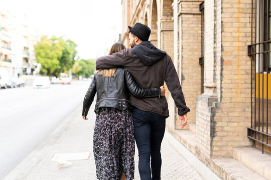 Back view of young couple in love walking arm in arm in the city