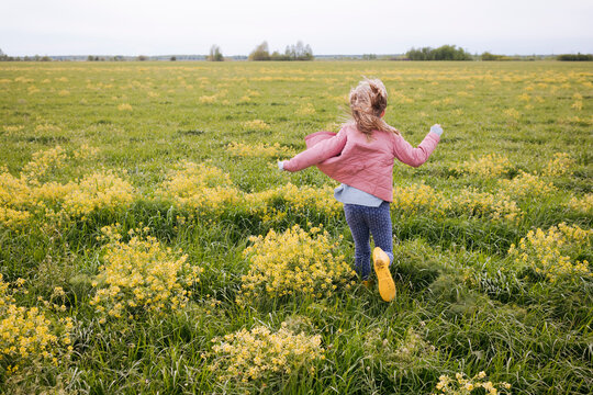 Girl in yellow rubber boots running near rape field