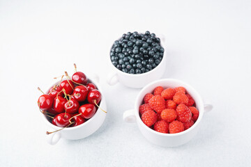 Bowls of raspberries, blueberries and cherries for fruit trio, diet or nutrition concept
