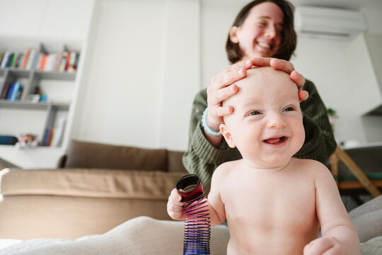 Playful mother with hands on head of baby sitting in living room at home