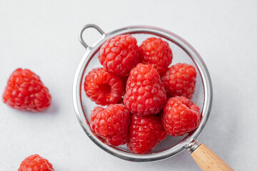 Raspberries in strainer on white background for cooking ingredient or minimal healthy snack concept