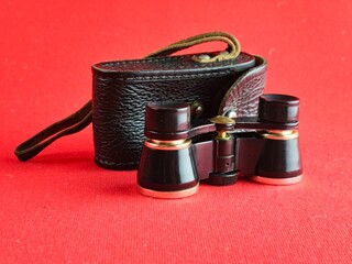 Vintage black theatre binoculars with black leather case on red background. Made in USSR. 1960s.