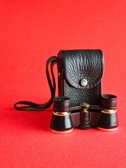 Vintage black theatre binoculars with a black leather case on red background. Made in USSR. 1960s.