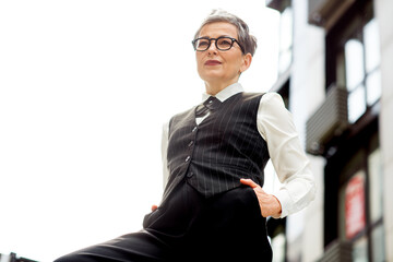 Elegant businesswoman standing outdoors in formal attire with a professional demeanor in an urban...