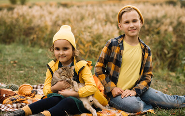 Little cute smiling girl and boy sitting on plaid with cat. Kid resting with her family in the nature. Picnic. Autumn season.