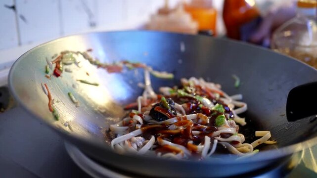 Soy sauce being poured into a wok with stir-fried noodles, vegetables, and meat, enhancing flavor and color.