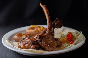 Rack of lamb with vegetables on a white plate on a black background