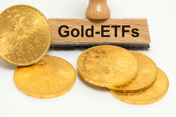 Ein Holzstempel ist beschriftet mit Gold-ETFs über echten Goldmünzen