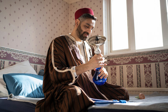 Man doing preparation of hookah while sitting on bed at home