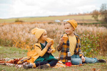 Little cute smiling girl and boy sitting on plaid and drinking cocoa. Kid resting with her family in the nature. Picnic. Autumn season.